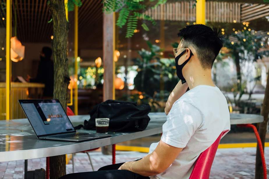 A man sitting in the outdoor section of a restaurant and working on his laptop with employee monitoring software.
