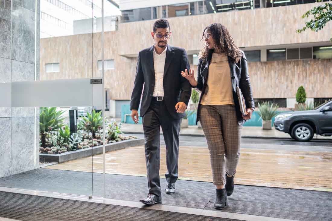 Two employees walking into an office building discussing their return to office strategy.