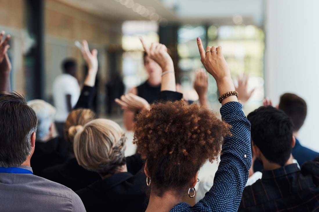 Employees raising their hands to monitor employee attendance at a meeting.