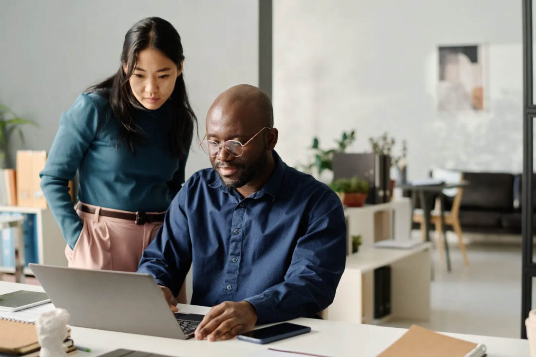 Two professionals in a modern office working together on a laptop.